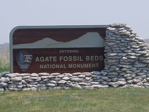 Sign marking the entrance to Agate Fossil Beds National Monument, featuring stone accents and grassy surroundings.