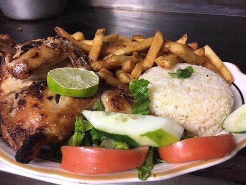 A plate of grilled chicken with lime, served with rice, lettuce, cucumber, tomato, and crispy French fries.