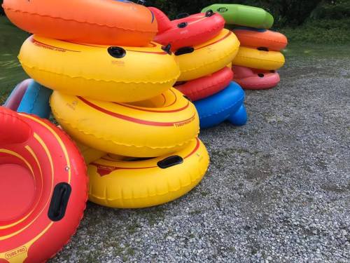 A stack of colorful inflatable tubes in various sizes, resting on gravel in a grassy area.