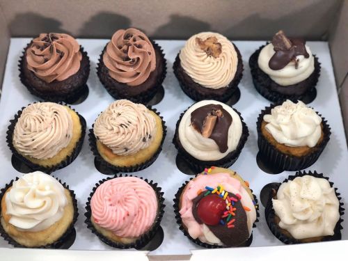 A box of assorted cupcakes featuring various flavors and toppings, including chocolate, vanilla, and sprinkles.