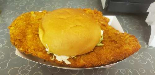 A large fried chicken sandwich with a golden bun and crispy chicken patty, served on a patterned table.
