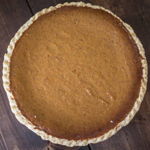 A freshly baked pumpkin pie with a golden crust, resting on a wooden surface.