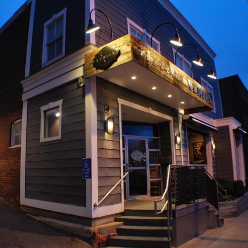 Exterior of a pizzeria at dusk, featuring a wooden sign, outdoor lighting, and accessible entrance.