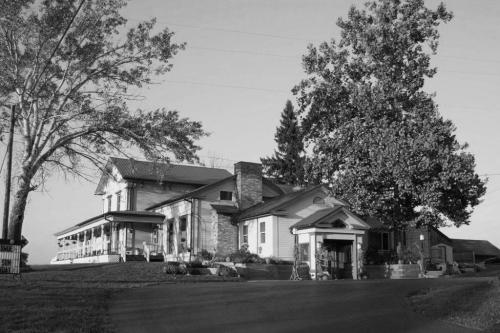 A large, historic house with a porch, surrounded by trees, captured in black and white.