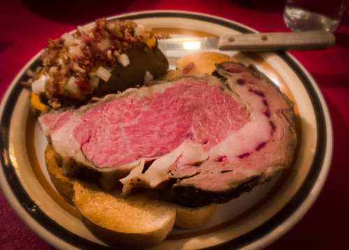 A plate featuring a thick slice of pink roast beef on bread, accompanied by a loaded baked potato.