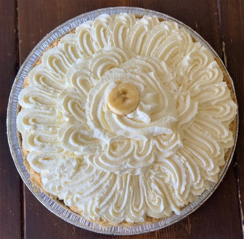 A round banana cream pie topped with swirls of whipped cream and a banana slice in the center.
