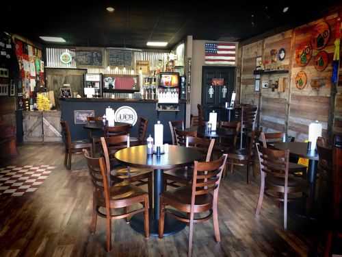 Cozy restaurant interior with wooden tables, chairs, and a rustic decor featuring an American flag and colorful wall art.