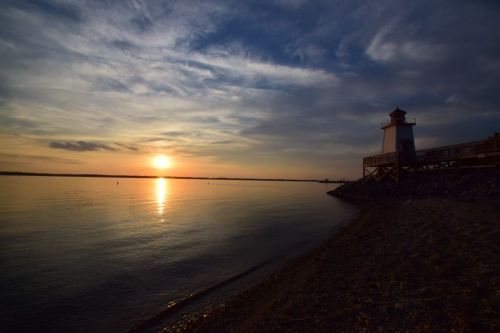 A serene sunset over calm waters, with a lighthouse silhouetted against the colorful sky.
