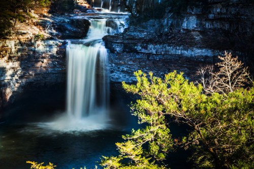 A serene waterfall cascades into a tranquil pool, surrounded by lush greenery and rocky cliffs.