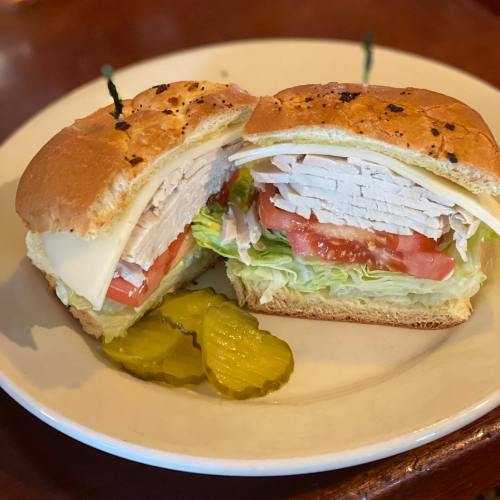 A sandwich with turkey, lettuce, tomato, and cheese, served with pickles on the side.