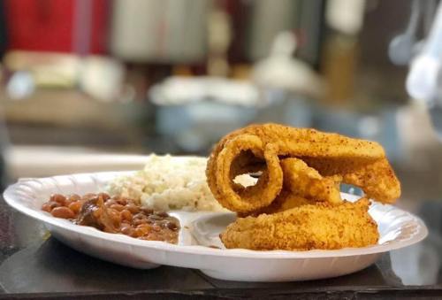 A plate with seasoned fried fish, rice, and baked beans, served on a disposable white plate.