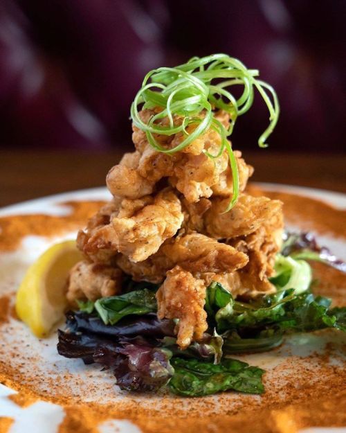 A stack of crispy fried chicken on a bed of greens, garnished with green onions and a lemon wedge.