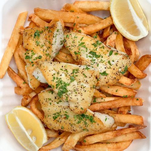 A serving of golden fries topped with crispy fried fish fillets and garnished with parsley and lemon wedges.
