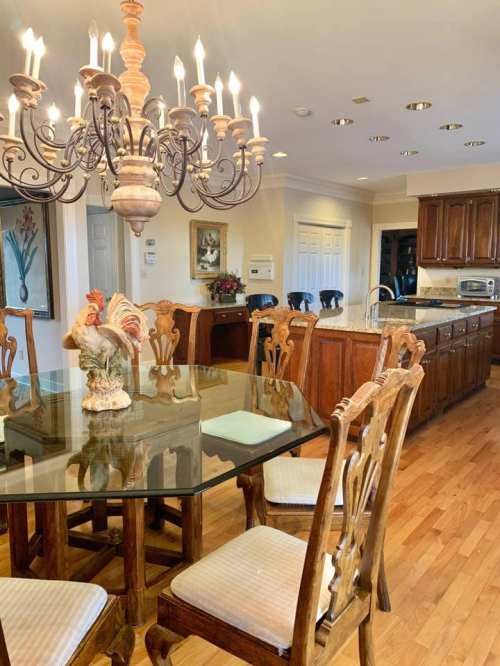 A dining area with a wooden table, elegant chairs, and a chandelier, featuring a decorative rooster centerpiece.