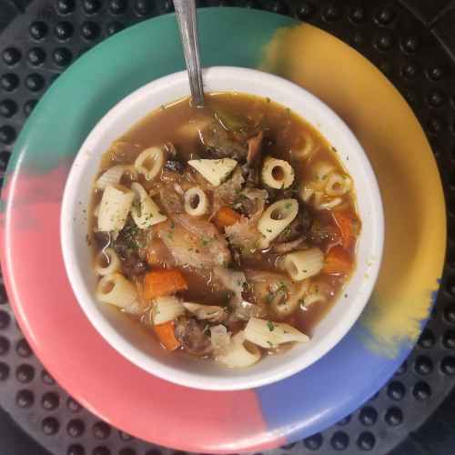 A bowl of soup with pasta, vegetables, and herbs, served on a colorful plate.