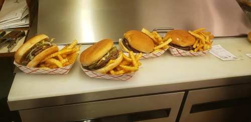 Four burgers with fries in red and white baskets on a countertop.