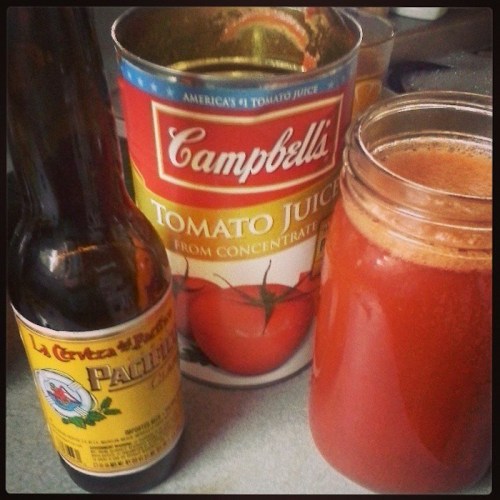 A bottle of beer next to a jar of tomato juice and a can of Campbell's tomato juice on a countertop.