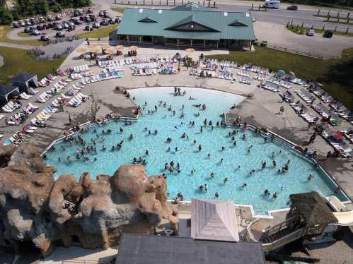 Aerial view of a large pool surrounded by lounge chairs, with many people swimming and relaxing in the water.