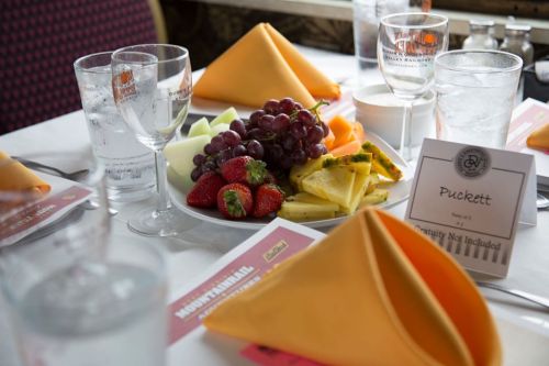 A table set with orange napkins, glasses, and a platter of fresh fruit including strawberries, grapes, and pineapple.