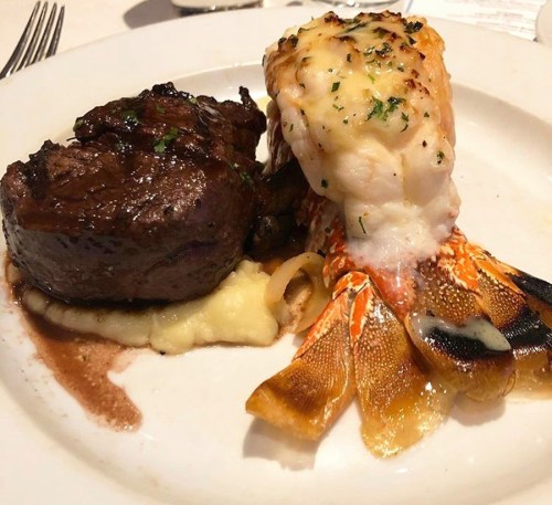 A plate featuring a filet mignon with mashed potatoes and a lobster tail, garnished with herbs.