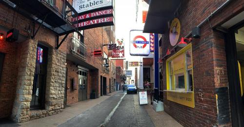 Narrow alleyway lined with brick buildings, featuring neon signs for bars and theaters, with a car parked at the end.