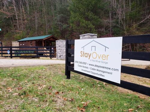 Sign for StayOver at Red River Gorge, featuring cabin rentals and management, with a rustic cabin in the background.