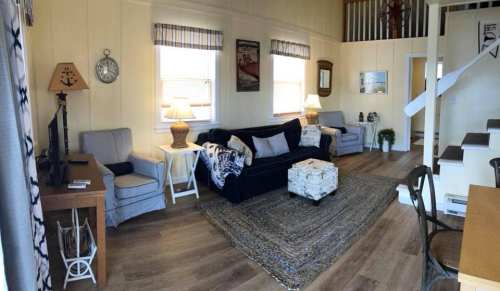 Cozy living room with a sofa, armchairs, lamps, and a decorative rug, featuring light wood flooring and nautical decor.