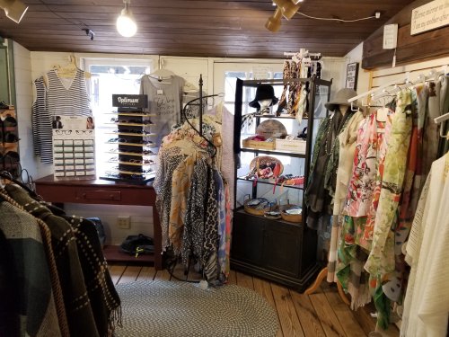A cozy shop interior featuring clothing racks, sunglasses, and accessories displayed on shelves and hangers.