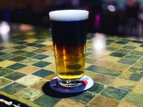 A pint of beer with a layered appearance, resting on a colorful tiled bar top.