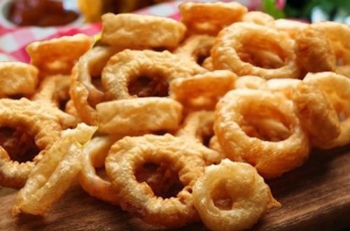 A close-up of golden-brown, crispy onion rings piled on a wooden surface.