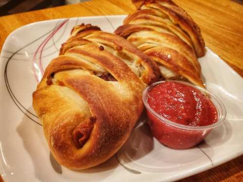 Two golden-brown calzones on a plate, served with a small cup of marinara sauce.