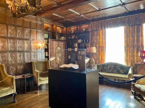 A cozy, vintage library with wooden paneling, bookshelves, elegant furniture, and warm lighting.