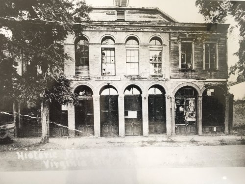 Black and white photo of a historic brick building with multiple doors and large windows, surrounded by trees.
