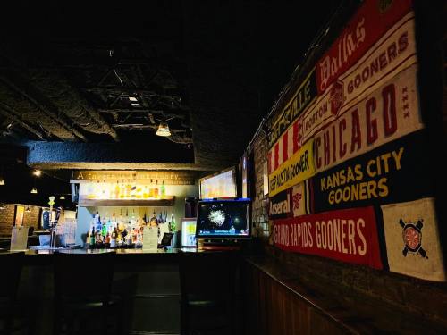 A cozy bar interior featuring a colorful wall of sports banners and a well-stocked bar in the background.