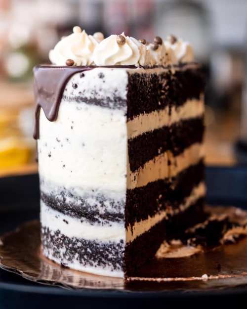 A layered chocolate cake with cream frosting and a chocolate ganache top, partially sliced to reveal its interior.
