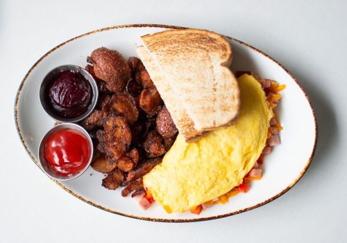 A plate featuring a fluffy omelet, crispy potatoes, toast, and two dipping sauces.