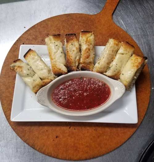 A plate of cheesy breadsticks arranged around a bowl of marinara sauce, garnished with herbs and cheese.