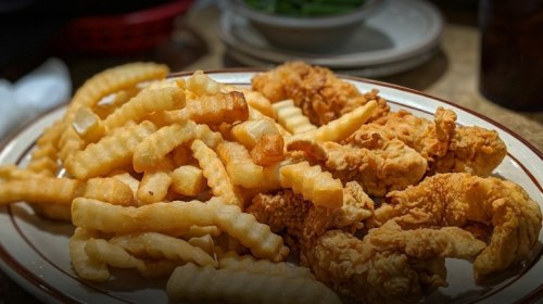 A plate of crispy fried chicken strips served with golden crinkle-cut fries.