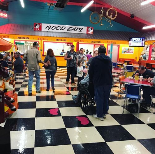 A colorful diner interior with people dining, a wheelchair user, and a sign reading "GOOD EATS" above the counter.