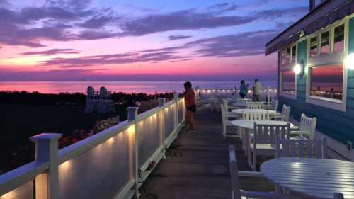 A serene sunset view from a deck, with people enjoying the scenery and colorful clouds reflecting over the water.