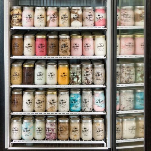 A refrigerator filled with various jars of colorful ice cream in different flavors, neatly arranged on shelves.