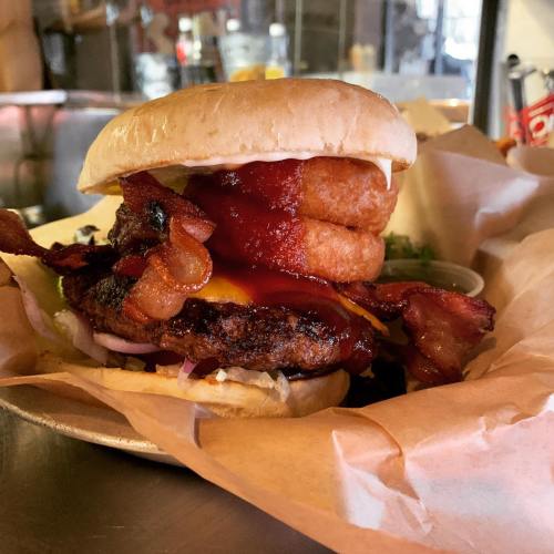 A hearty burger stacked with bacon, cheese, and onion rings, served in a bun with condiments on a plate.