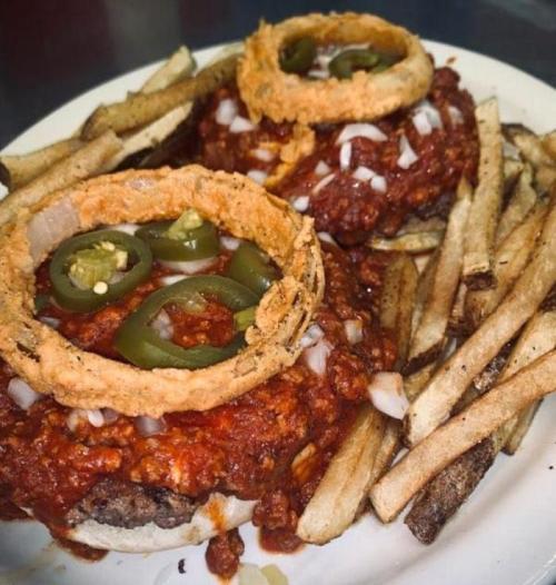 Two burgers topped with chili, jalapeños, and onion rings, served with a side of crispy French fries.