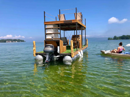 A floating wooden structure on clear water, with a person kayaking nearby under a blue sky.