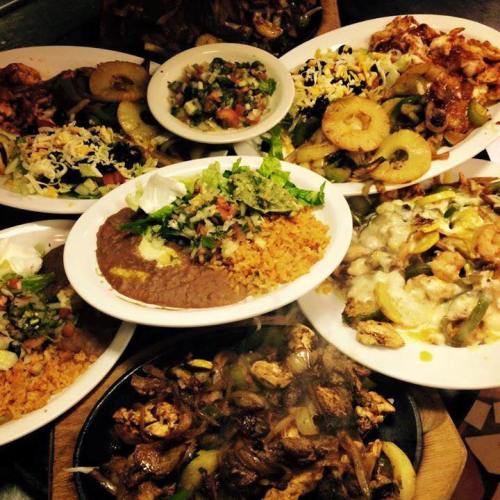 A vibrant spread of Mexican dishes, including fajitas, rice, beans, and fresh salads, served on white plates.