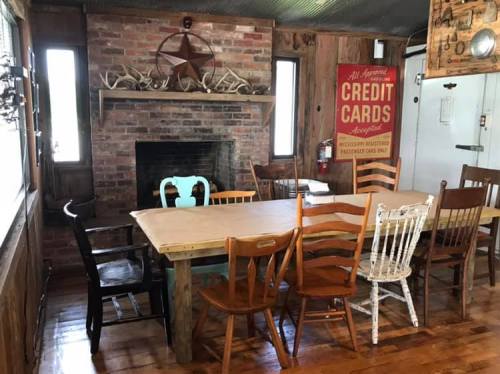 Cozy dining area with a large wooden table, various chairs, a brick fireplace, and rustic decor on the walls.