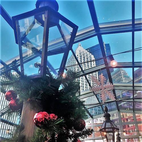 A festive scene featuring holiday decorations, lanterns, and a view of skyscrapers through a glass ceiling.