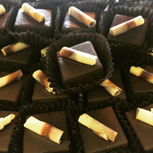 A close-up of assorted chocolate confections, topped with small white and brown striped chocolate pieces.