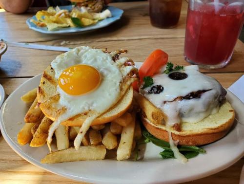 A plate with a burger topped with melted cheese and a fried egg, served with fries and a slice of tomato.