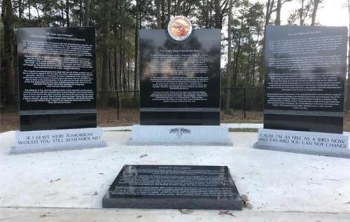 Three black granite memorial panels with inscriptions, surrounded by trees in a park setting.